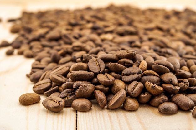 Photo brown coffee beans on yellow textured wooden board background close up.