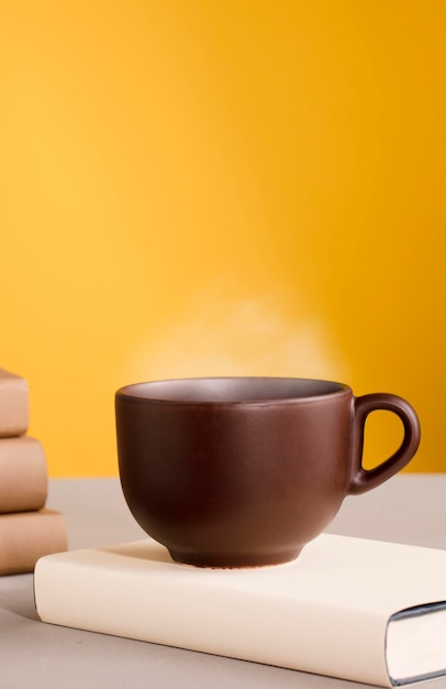 Brown cup of coffee or tea with hot steam and books orange\
yellow background