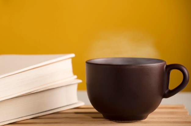 Brown cup of coffee or tea with hot steam on the table with books