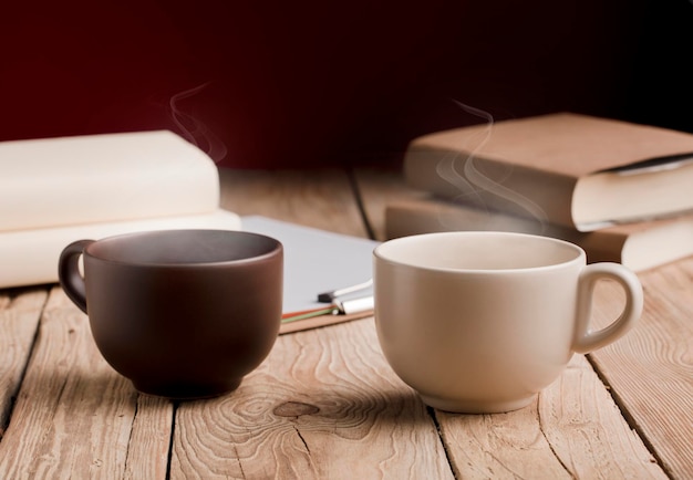 brown cup and white cup with chocolate tea or coffee hot steam books on rustic wooden table