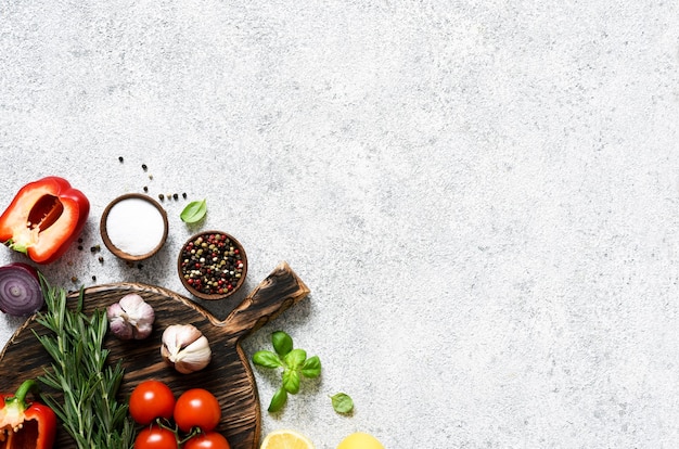 Brown cutting board with spices and vegetables on a light, a concrete kitchen table.