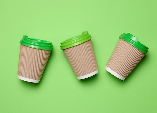 Brown disposable coffee and tea cups made of corrugated cardboard with green plastic lids on green background top view