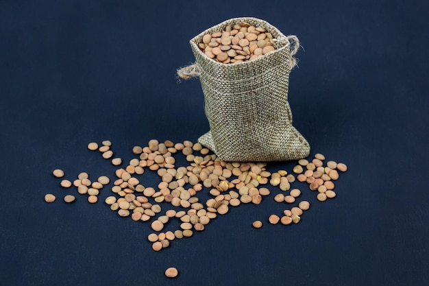 Brown dried lentils in a burlap bag on black background