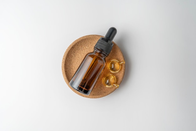 A brown dropper bottle and golden capsules for face care lying on a cork plate