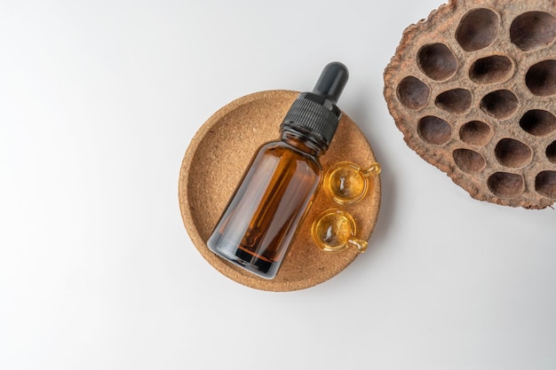 A brown dropper bottle and golden capsules for face care lying on a cork plate