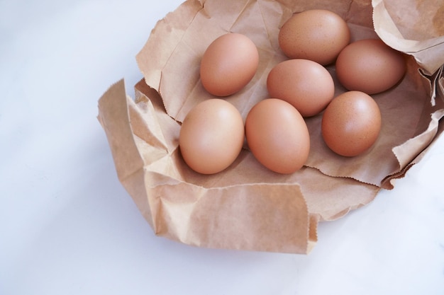 밝은 색 배경에 있는 종이 봉지에 있는 갈색 계란 나무 탁자에 있는 신선한 닭고기 달걀