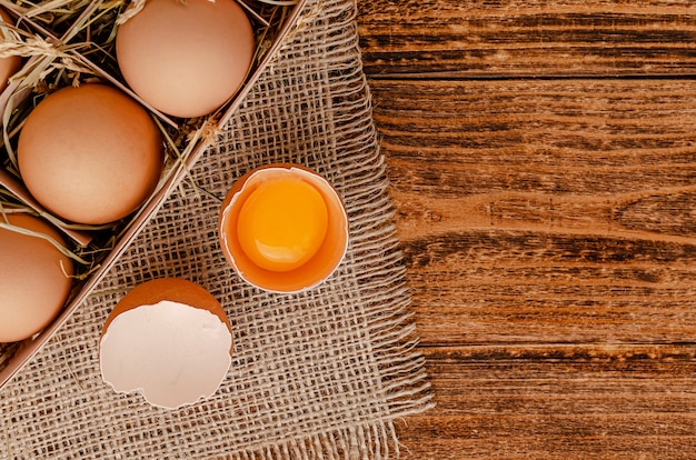 Brown eggs and broken egg with yolk on wooden