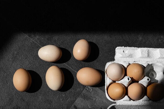 Photo brown eggs in carton box on dark background