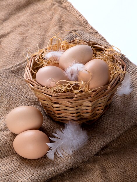 Фото Коричневые яйца на сене в гнезде с перьями. на фоне мешковины. вертикальная.