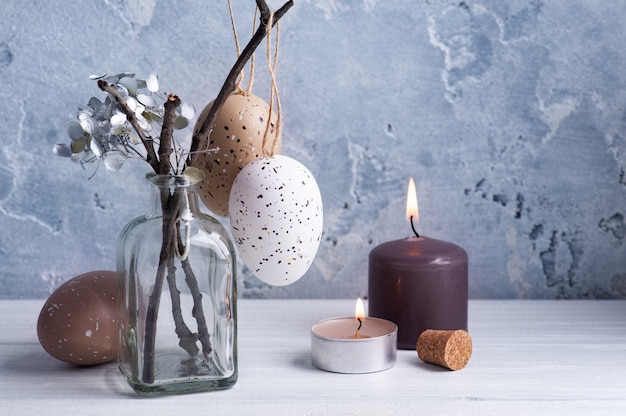 Brown eggs and lit candles in rustic Easter composition on white wooden table.