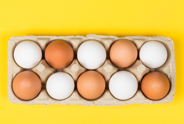 Brown eggs among white eggs in box on yellow background