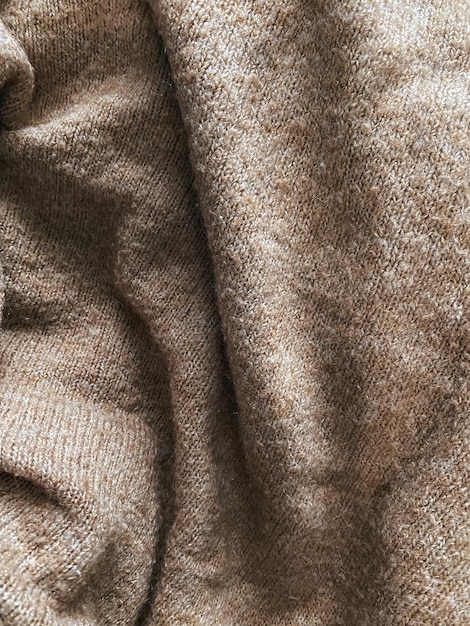 Brown fabric cloth texture background with wavy folds and shadows, closeup, vertical photo