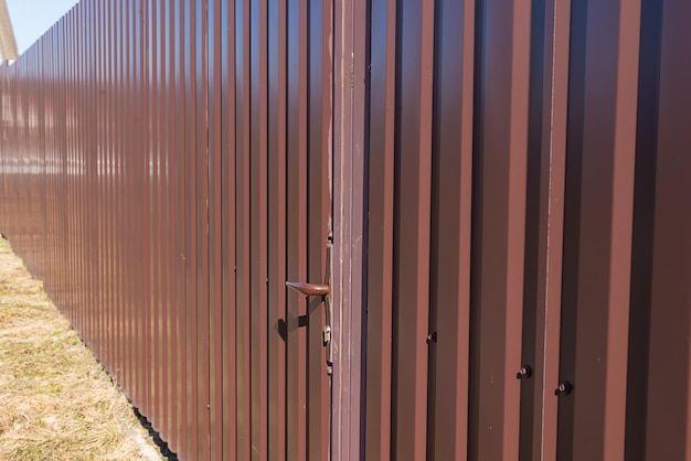 Brown fence made of metal profiles with a door Corrugated surface Security Private property fencing