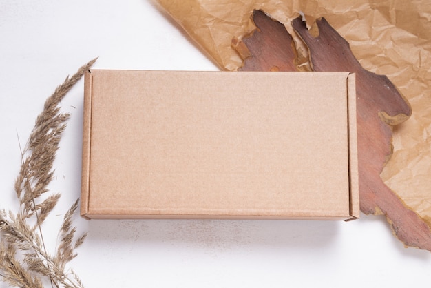 Photo brown flat cardboard carton box decorated with dried leaves, top view