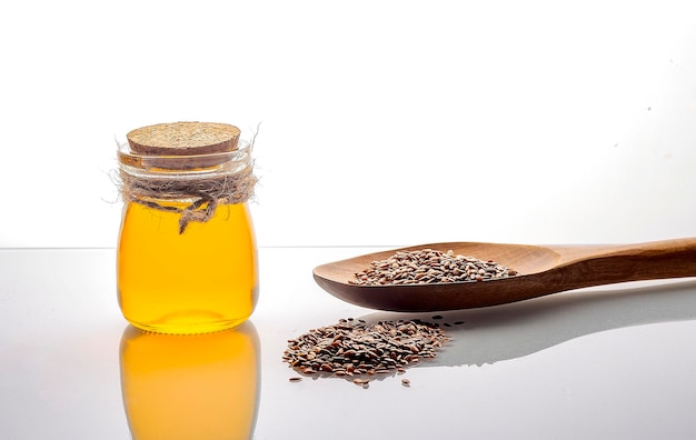 Brown flax seeds on a spoon and linseed oil in a glass jug on a white background