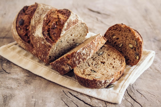 Brown fresh bread with seeds are cut into pieces on old wood background. Top view, copy space