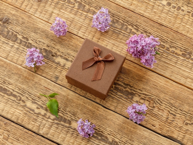 Brown gift box and lilac flowers on wooden boards. Top view. Greeting card concept.