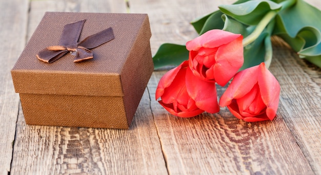 나무 판자에 아름다운 빨간 튤립이 있는 갈색 선물 상자. 휴일에 선물을 주는 개념.