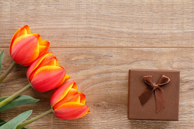 Brown gift box with beautiful red tulips on the wooden boards Top view Concept of giving a gift