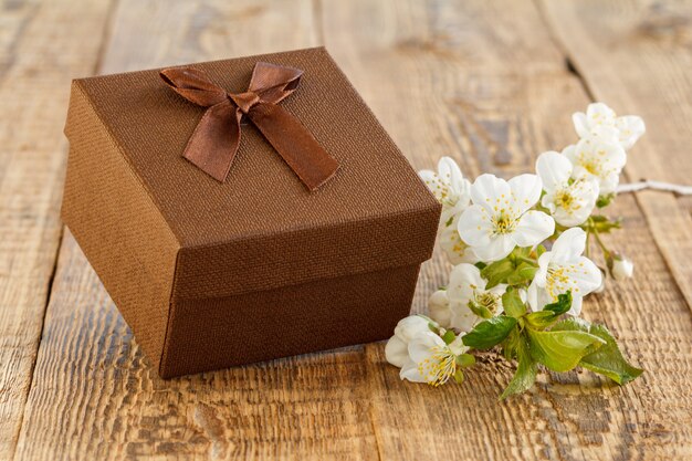 Brown gift box with branch of beautiful jasmine flowers on wooden boards. Concept of giving a gift on holidays.