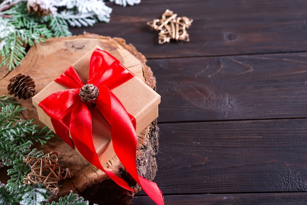 Brown gift box with red bow, christmas decoration on a wood cutting board on dark wooden , top view