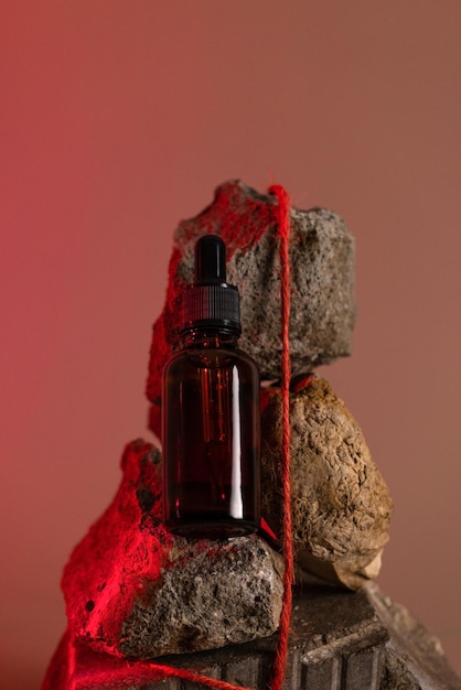 Brown glass bottle of cosmetic product or oil on stone in red light background futuristic cosmetic b...