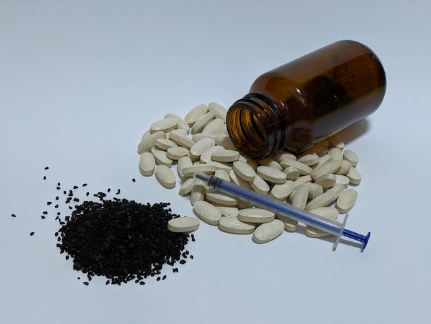 A brown glass bottle with grey pills and black seeds on isolated background