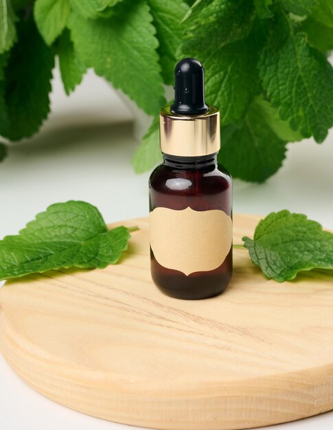 Brown glass bottle with paper label and pipette on a white table green mint leaves