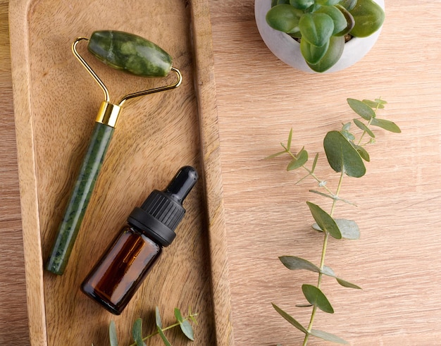 Brown glass bottle with pipette and green stone roller massager on a brown wooden background top view