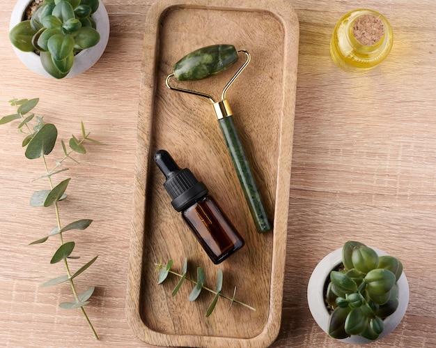 Brown glass bottle with pipette and green stone roller massager on a brown wooden background