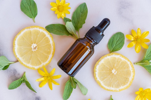 Brown glass bottle with a pipette, slices of lemon with mint leaves on a marble background