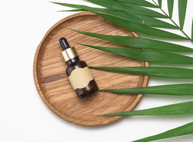 Brown glass bottle with a pipette and with blank paper label on a white background Container for cosmetics serum and oil palm leaf