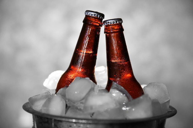 Photo brown glass bottles of beer in icepail on grey background