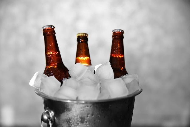 Коричневые стеклянные бутылки пива в ледяном ведре на сером фоне