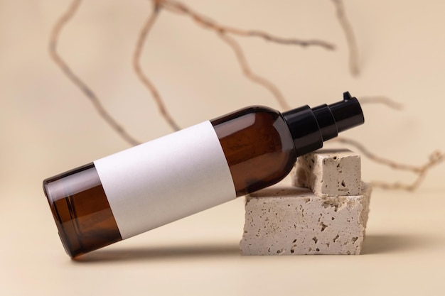 Brown glass cosmetic bottle lies on beige stones on light yellow Mockup