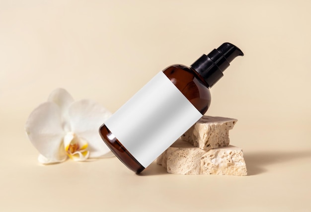 Brown glass cosmetic bottle near white orchid flower and stones on light yellow Mockup