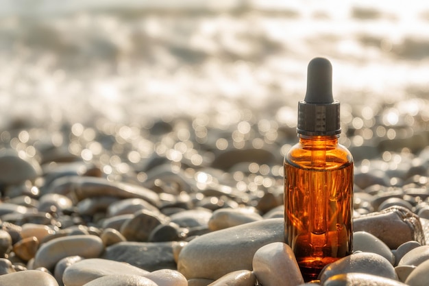 Flacone cosmetico in vetro marrone con pipetta nera sulla spiaggia di ciottoli di pietra in una giornata di sole. concetto di bellezza naturale.