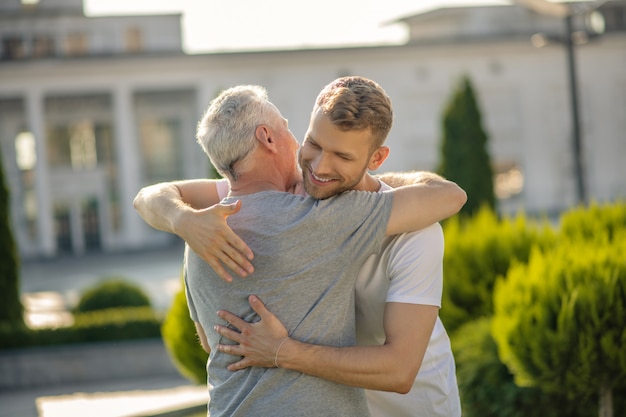 Brown-haired male and mature grey-haired male embracing each other