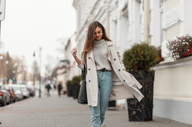 brown-haired woman in spring clothes and sneakers with a leather bag posing along the street