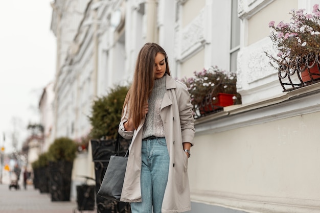 brown-haired woman in spring clothes and sneakers with a leather bag posing along the street