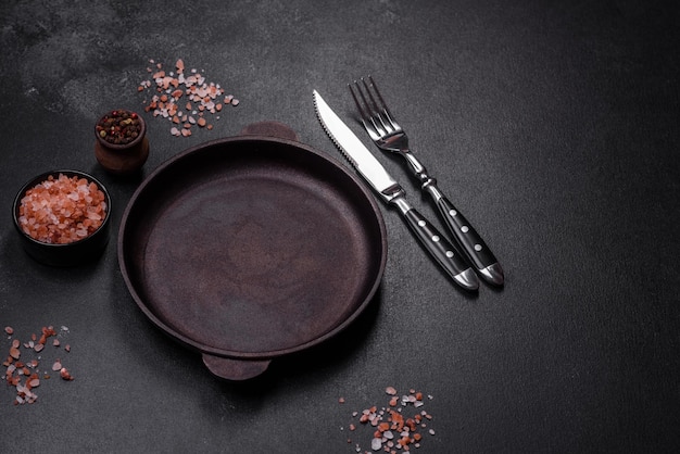 Brown iron empty pan with kitchen utensils on a dark concrete background