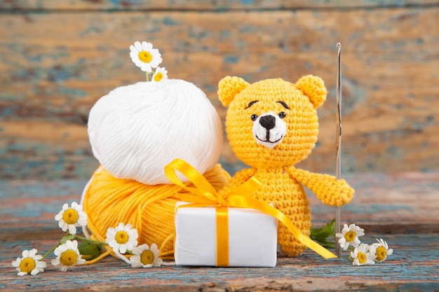 Фото Коричневый вязаный маленький медведь с ромашкой на старый деревянный. ручная вязаная игрушка. amigurumi
