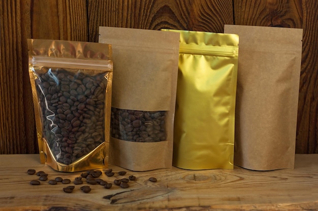 Brown kraft paper and golden metallized pouch bags with coffee beans front view on a wooden background