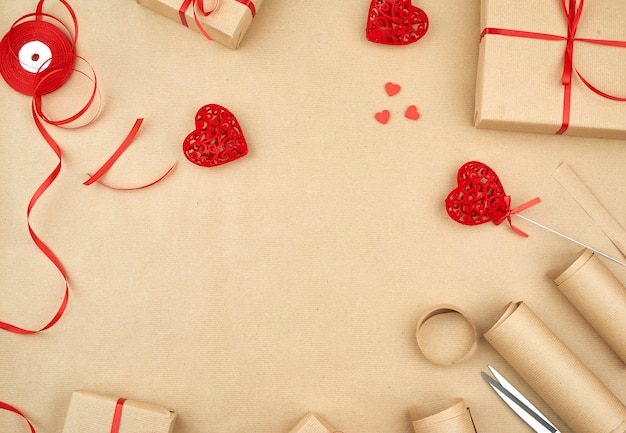 Коричневая крафт-бумага, упакованные подарочные пакеты и перевязанные красной ленточкой на красном фоне сердца