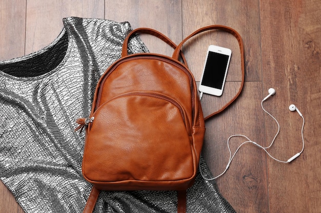 Brown leather backpack with female items on wooden surface top view