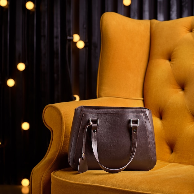 Brown leather bag for business woman on yellow armchair.