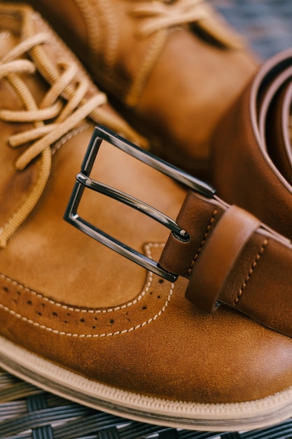 Коричневый кожаный ремень с металлической пряжкой на мужских коричневых ботинках со шнурками