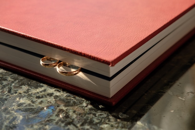 Коричневый кожаный обтянутый свадебный альбом с парой обручальных золотых колец, торцом.