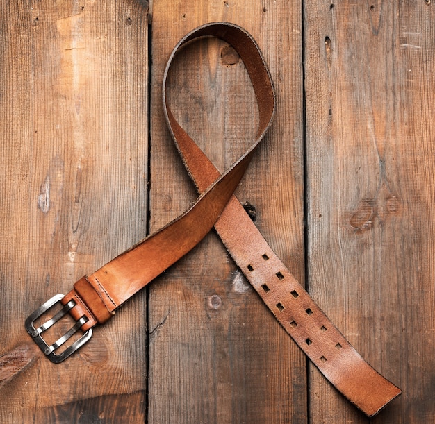 Brown leather men's belt with metal buckle on a wooden surface, top view