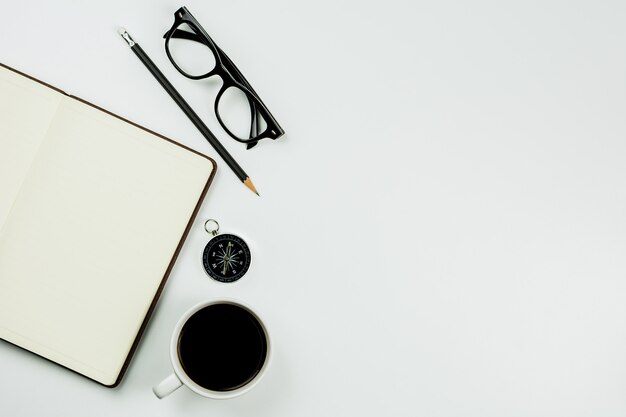 Brown leather notebook and a coffee cup on white desk background with copy space.